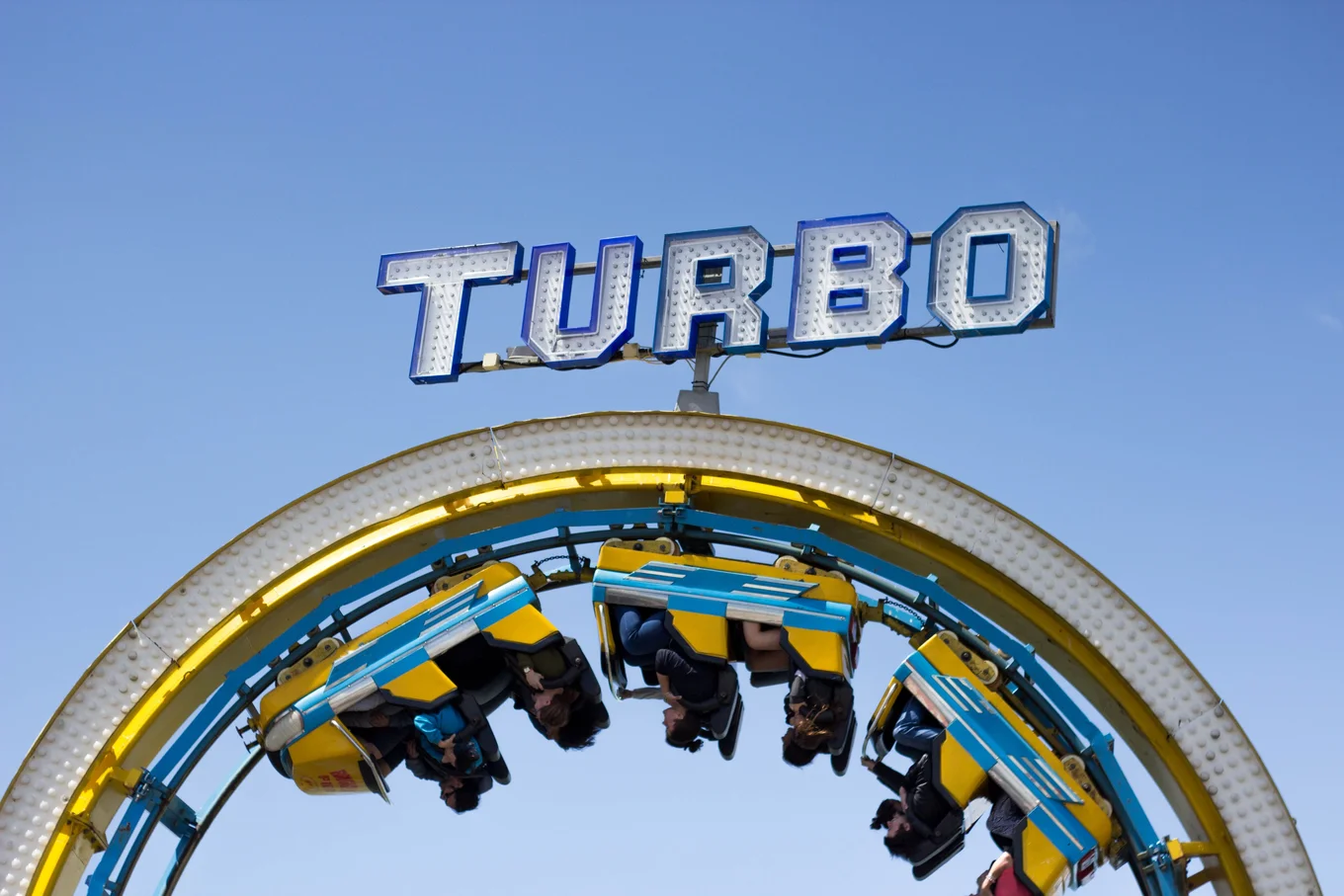 Roller coaster, upside-down, "TURBO" sign, blue sky.