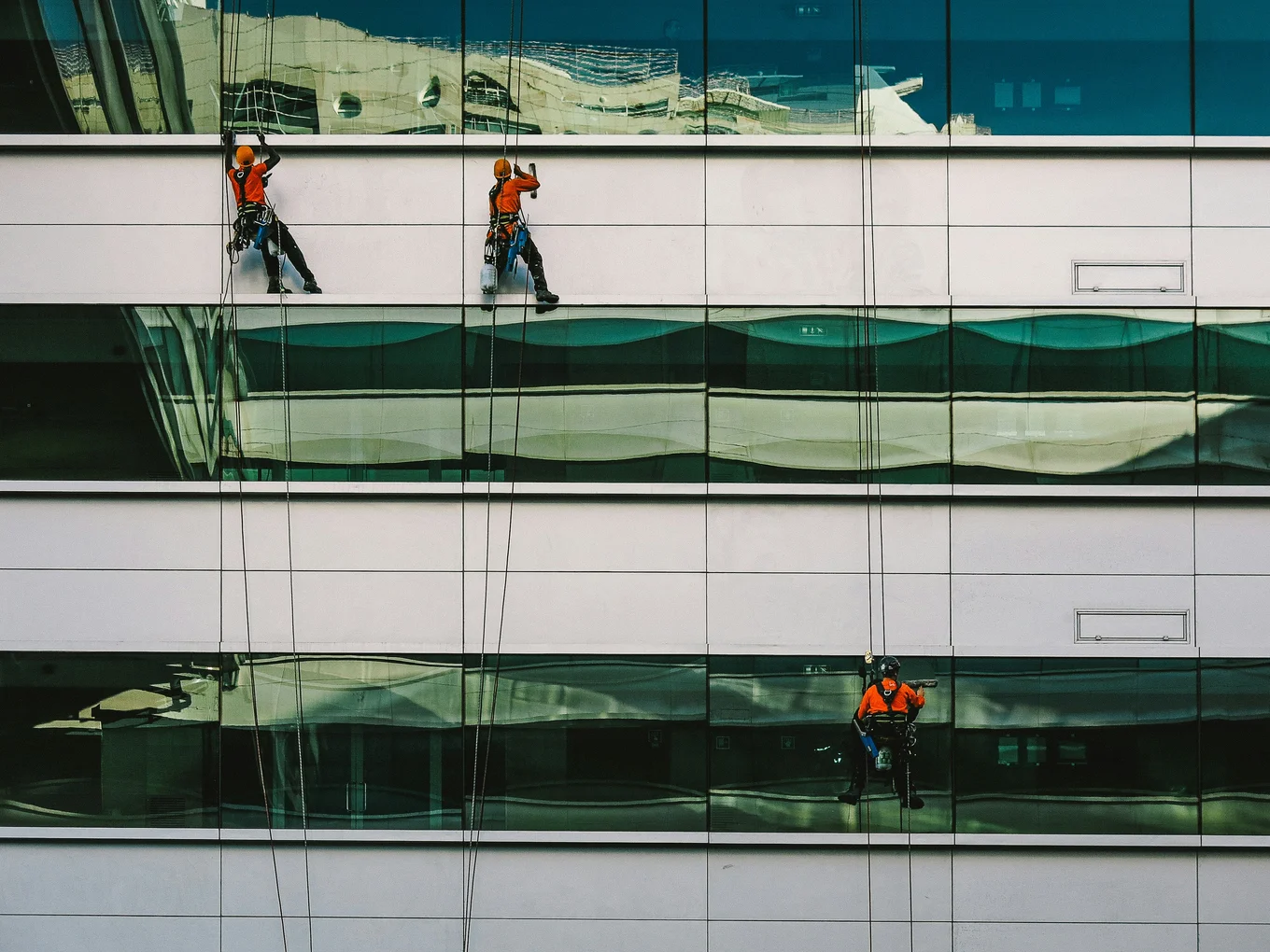 Three workers in orange harnessed on glass building.