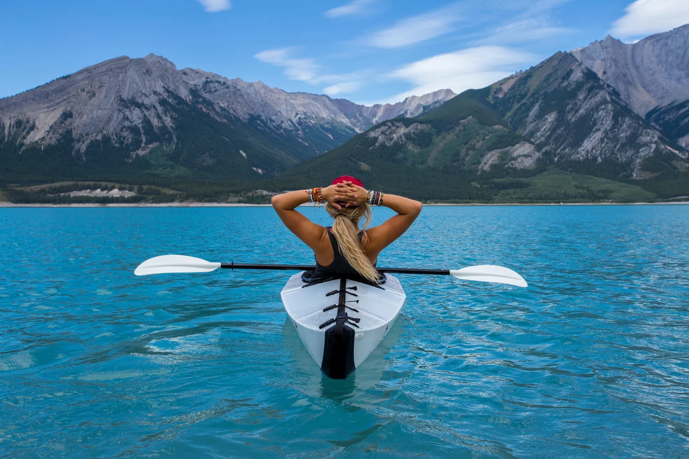 Person kayaking on a blue lake with mountains.